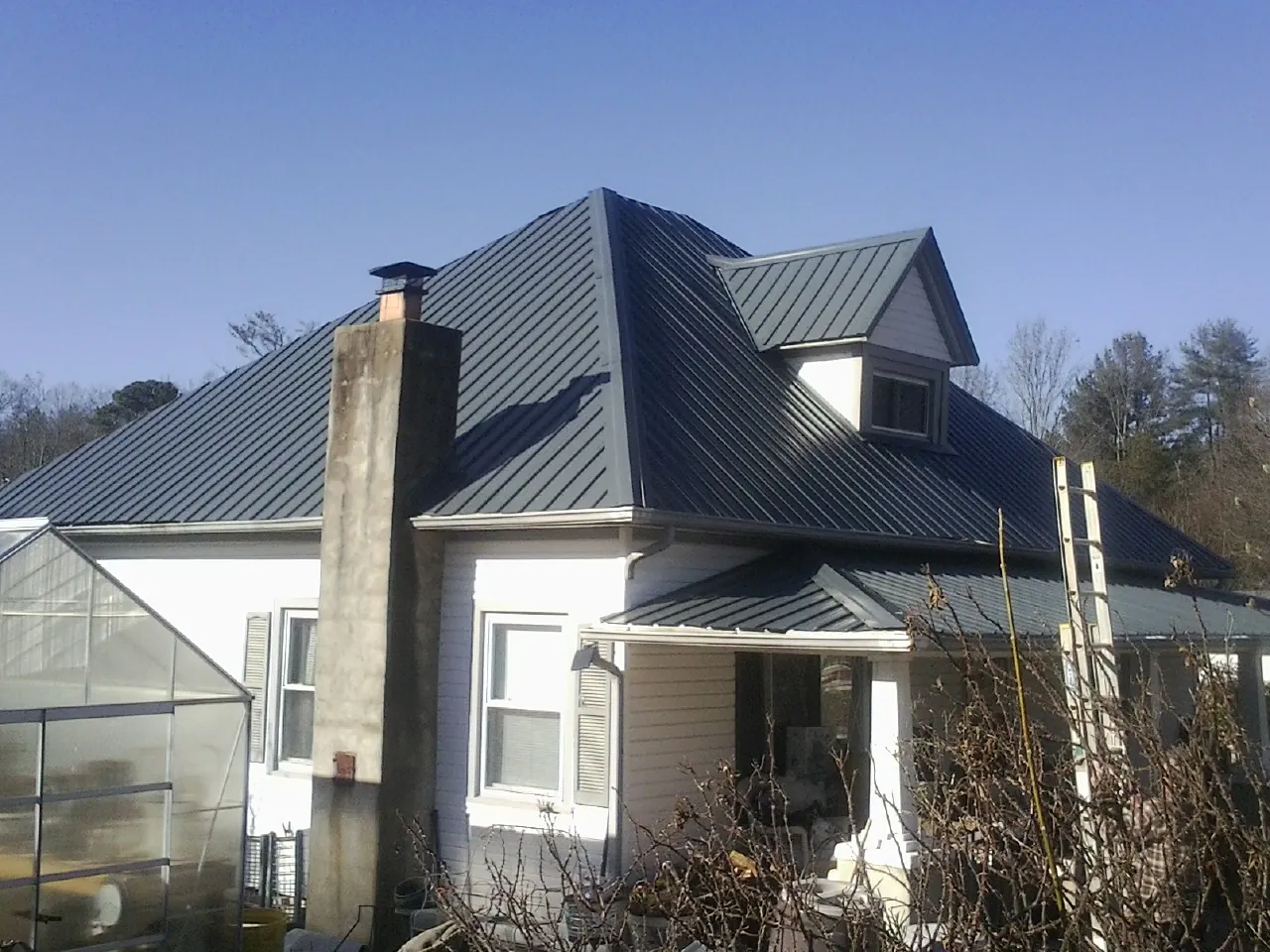 Dark blue standing seam metal roof on a white farmhouse with dormer — Slate & Tile Roof Repair by Roofing Brothers in Goodrich
