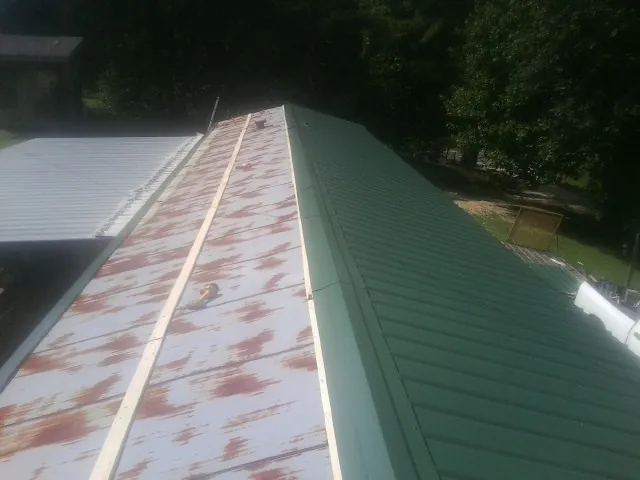 Old rusted panels beside newly installed green metal roofing — Wind Damage Roof Repair by Roofing Brothers in Goodrich