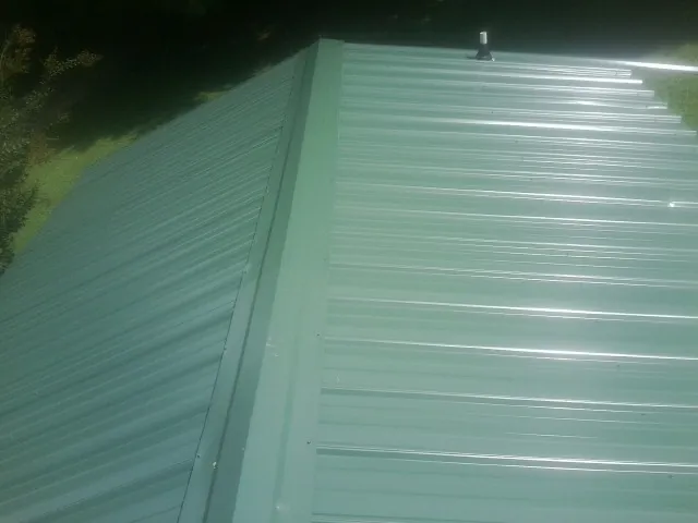 New green metal panels meeting at the ridge of a roof — Flat Roof Repair work by our crew in Goodrich