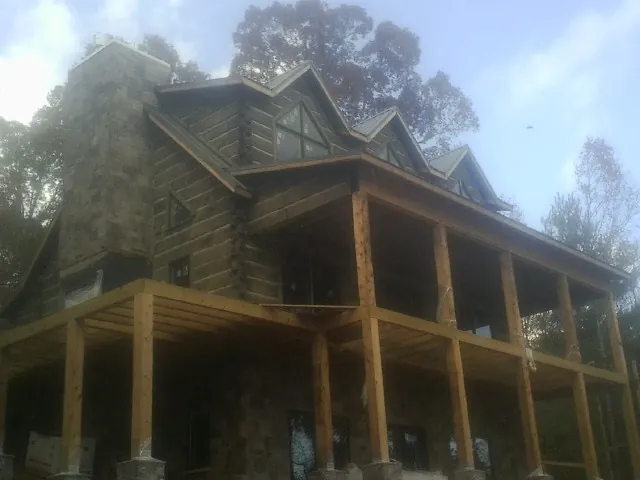 Stone chimney and dormers on a large log home with a timber porch in Goodrich